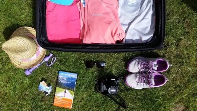 Un sac de voyage ouvert avec des vêtements, des chaussures, un chapeau, des lunettes de soleil et un appareil photo