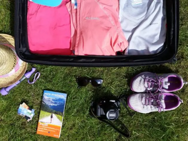 An open travel bag with clothes, shoes, a hat, sunglasses, and a camera