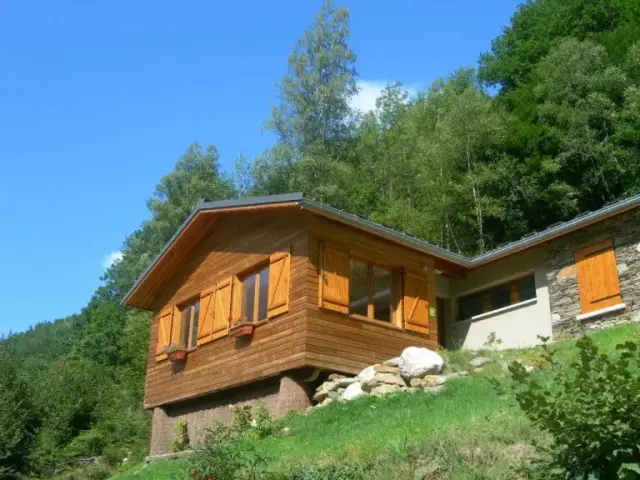 Wooden house with orange shutters on a green hillside