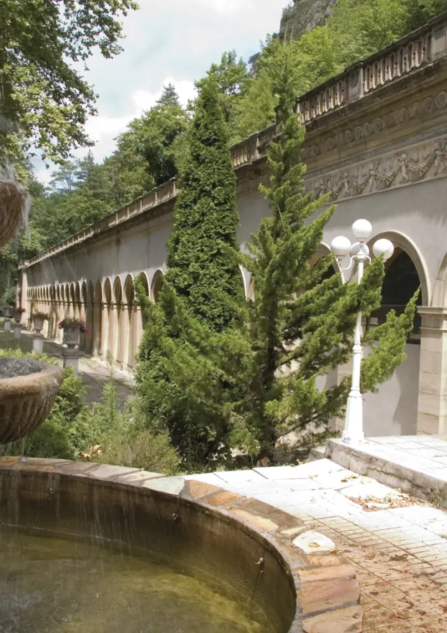 Fontaine avec de l'eau qui coule dans un jardin avec des plantes et un bâtiment en arrière-plan