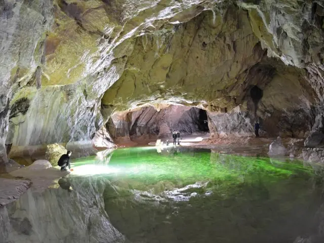 Explorers in a cave with a green light emanating from a pool