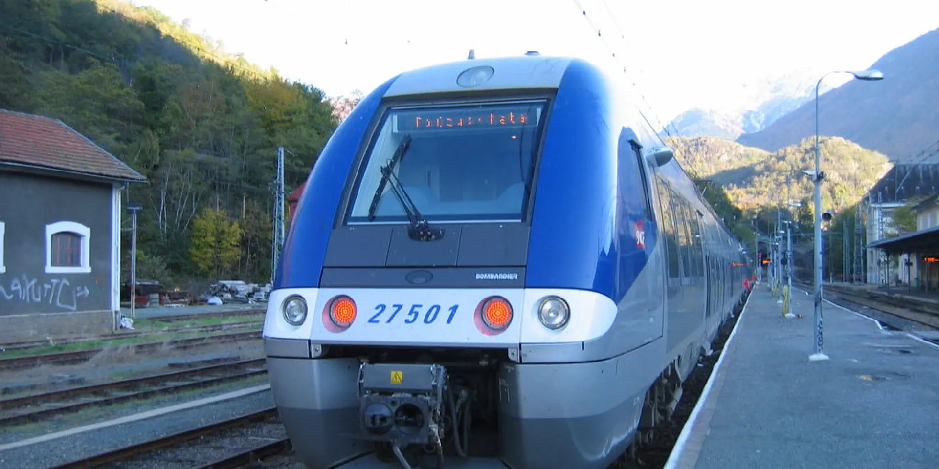 Blue and gray train at the station with mountains in the background