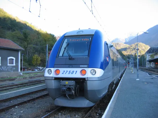 Train bleu et gris à la gare avec des montagnes en arrière-plan