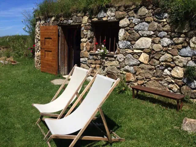 Cabaña de piedra con dos sillas de playa blancas y un banco de madera