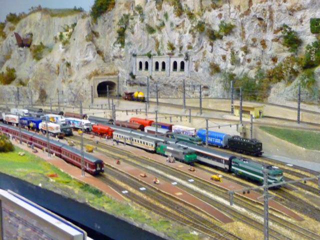 Several miniature trains running on tracks in a mountainous setting with a tunnel