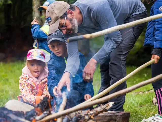 An adult and two children roasting marshmallows over an outdoor campfire