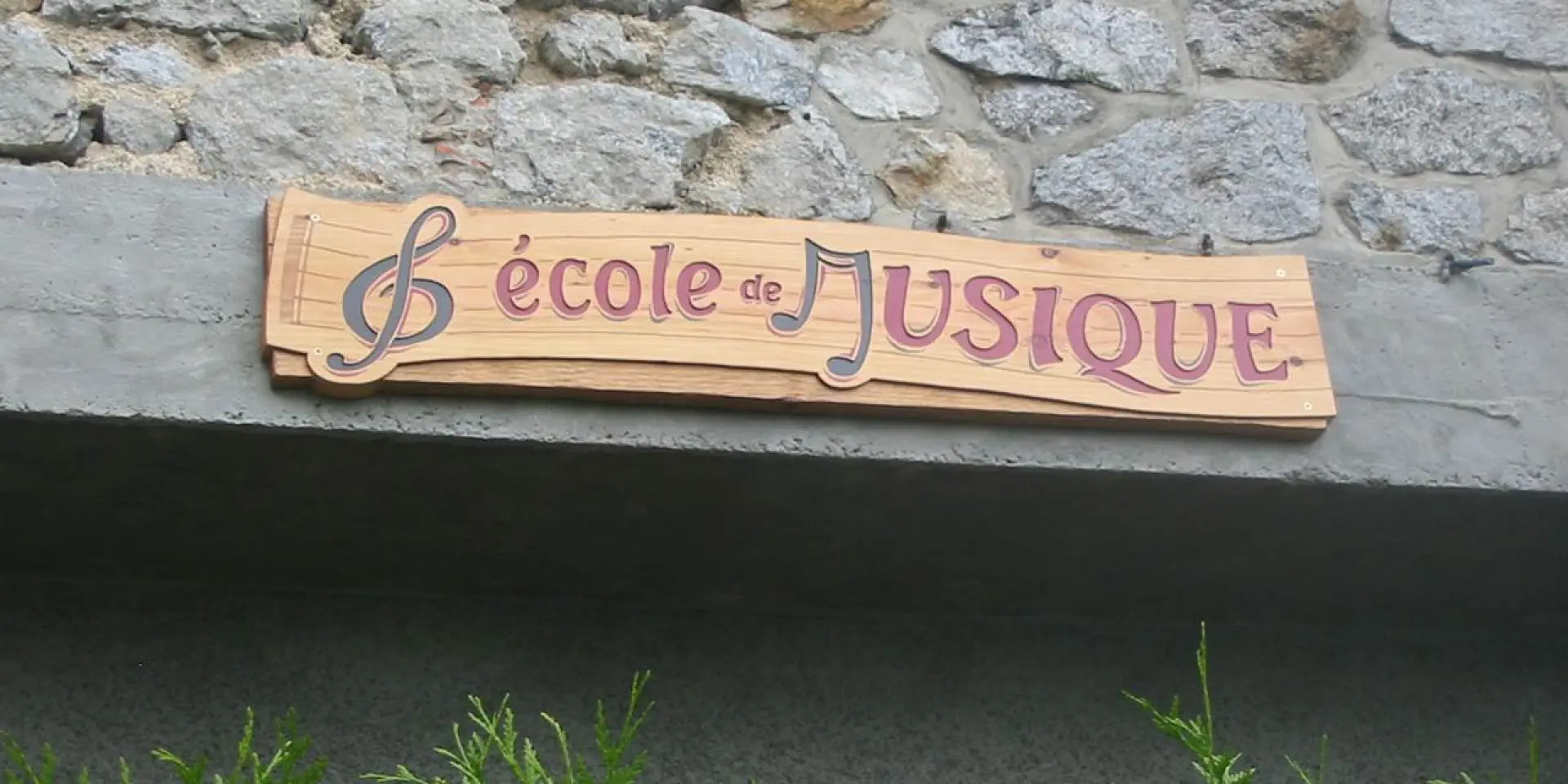 Señal de madera que indica Escuela de música frente a un muro de piedra