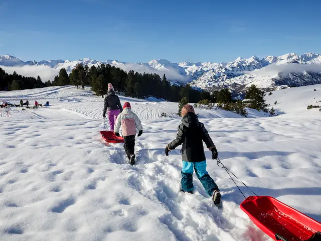Children pulling sleds on a snowy slope with mountains in the background