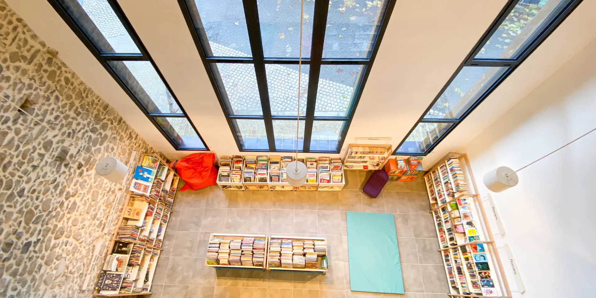 Intérieur d'une bibliothèque avec des étagères remplies de livres et de grandes fenêtres laissant entrer la lumière naturelle