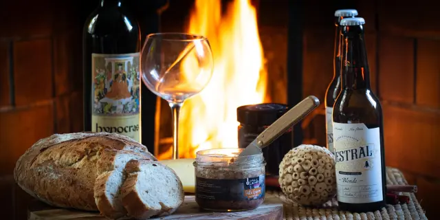 A platter with bread, wine, beer, and accompaniments in front of a fireplace