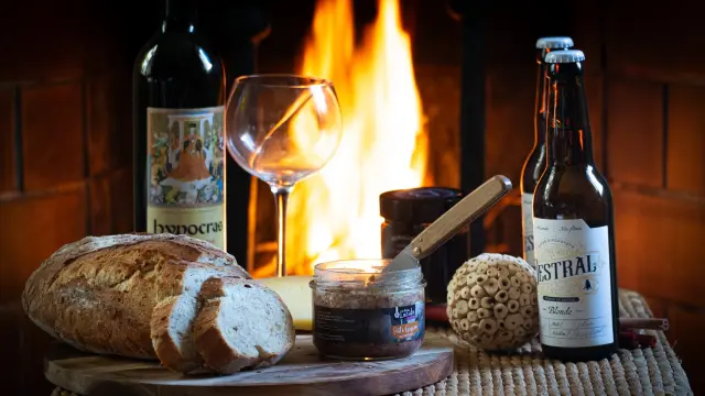 A platter with bread, wine, beer, and accompaniments in front of a fireplace