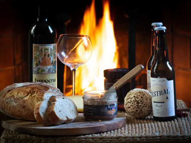 Una bandeja con pan, vino, cerveza y acompañamientos frente a una chimenea