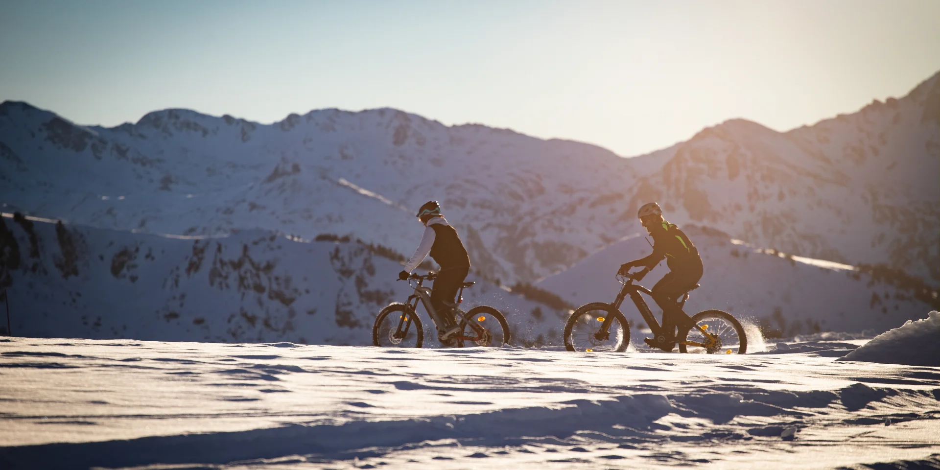 Deux personnes faisant du vélo dans un paysage enneigé avec des montagnes en arrière-plan
