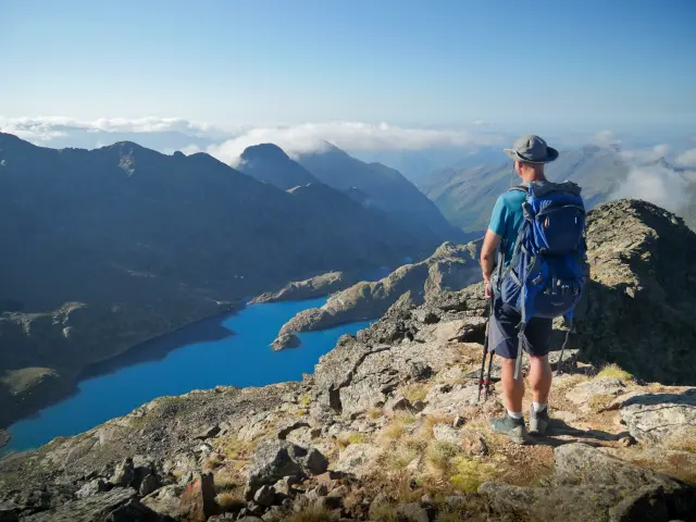 A hiker with a backpack on a mountain trail overlooking a lake