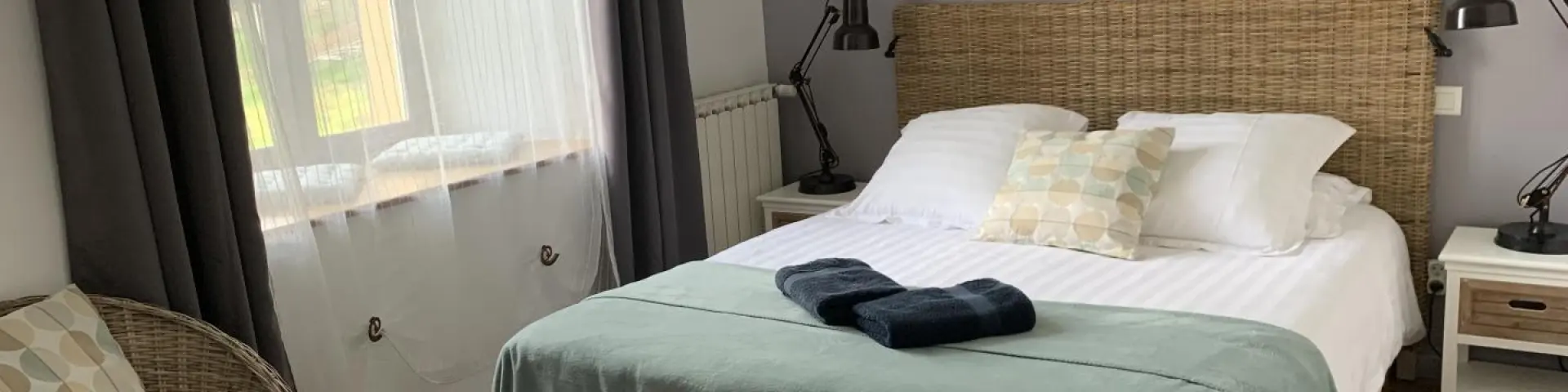 Dormitorio con cama doble, manta verde, dos lámparas de mesa y una ventana con cortinas grises