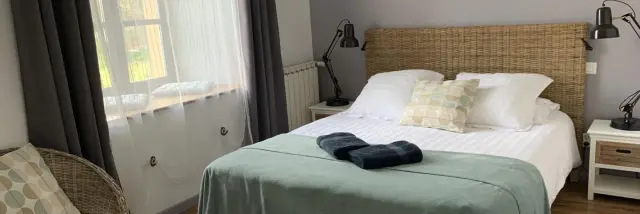 Bedroom with double bed, green blanket, two bedside lamps, and a window with gray curtains