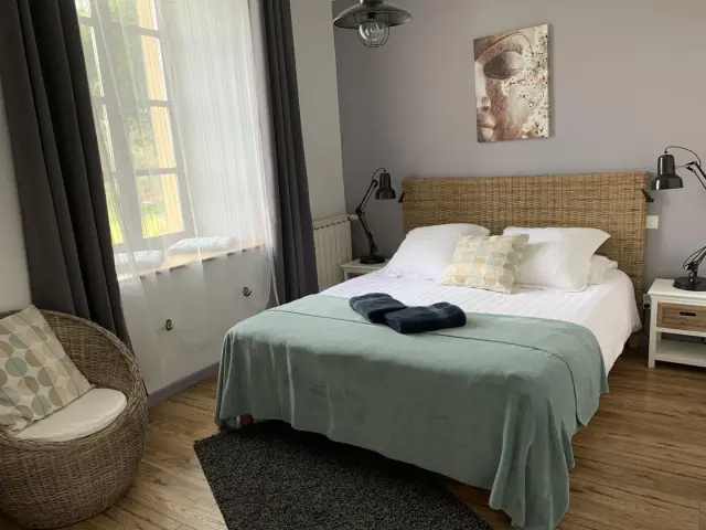 Bedroom with double bed, green blanket, two bedside lamps, and a window with gray curtains