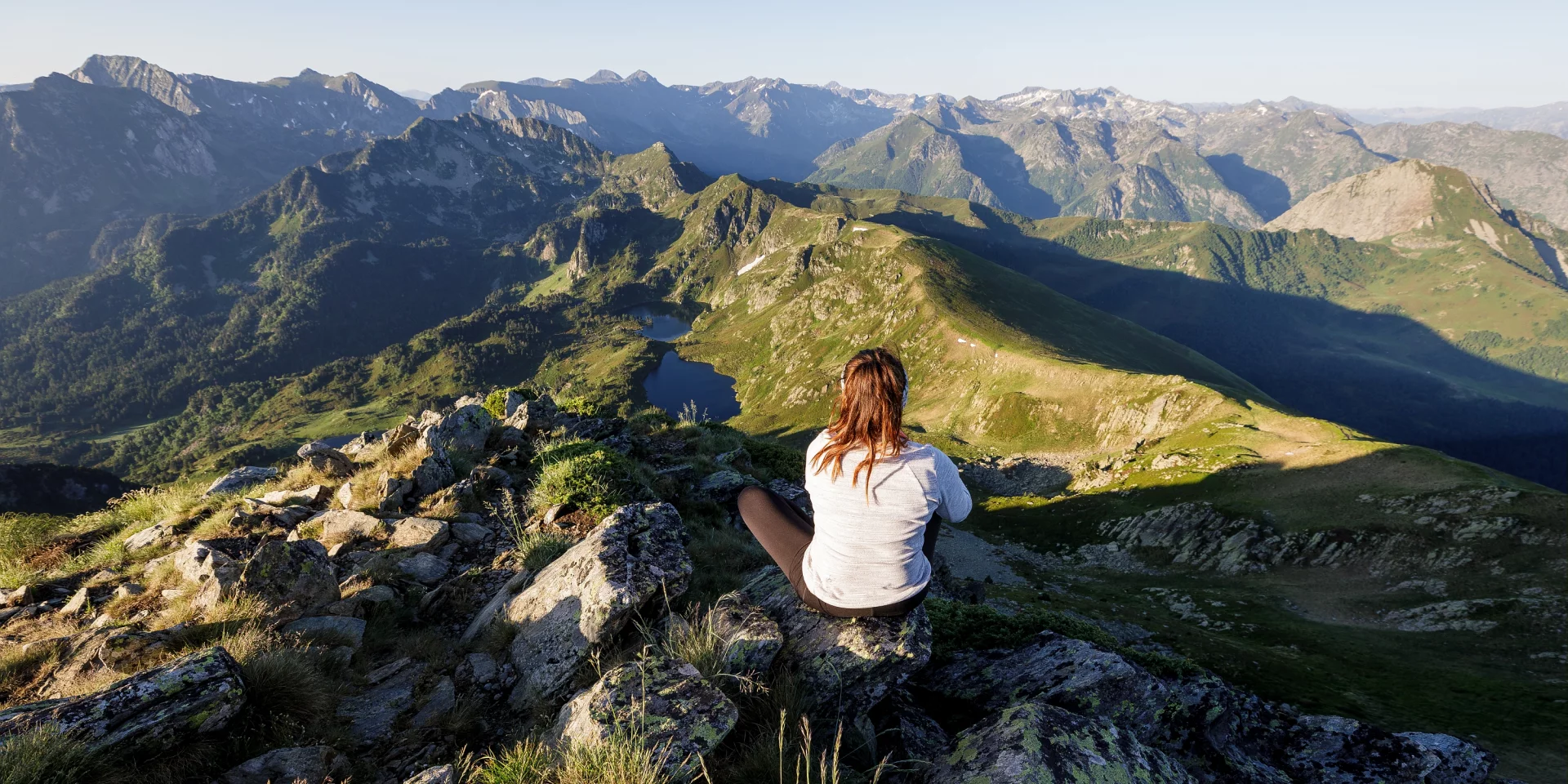 A woman sitting cross-legged on a rock in the mountains