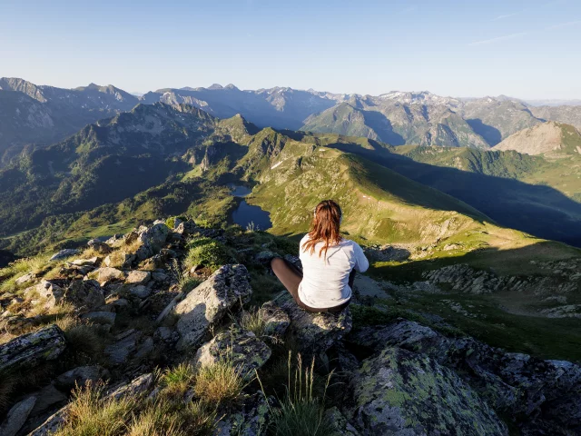 A woman sitting cross-legged on a rock in the mountains