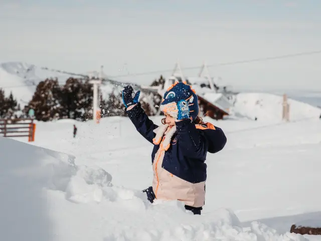Niño vestido abrigado jugando en la nieve con guantes y una bufanda
