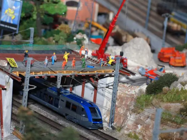 Workers in high visibility gear working on a bridge under construction with a train passing underneath